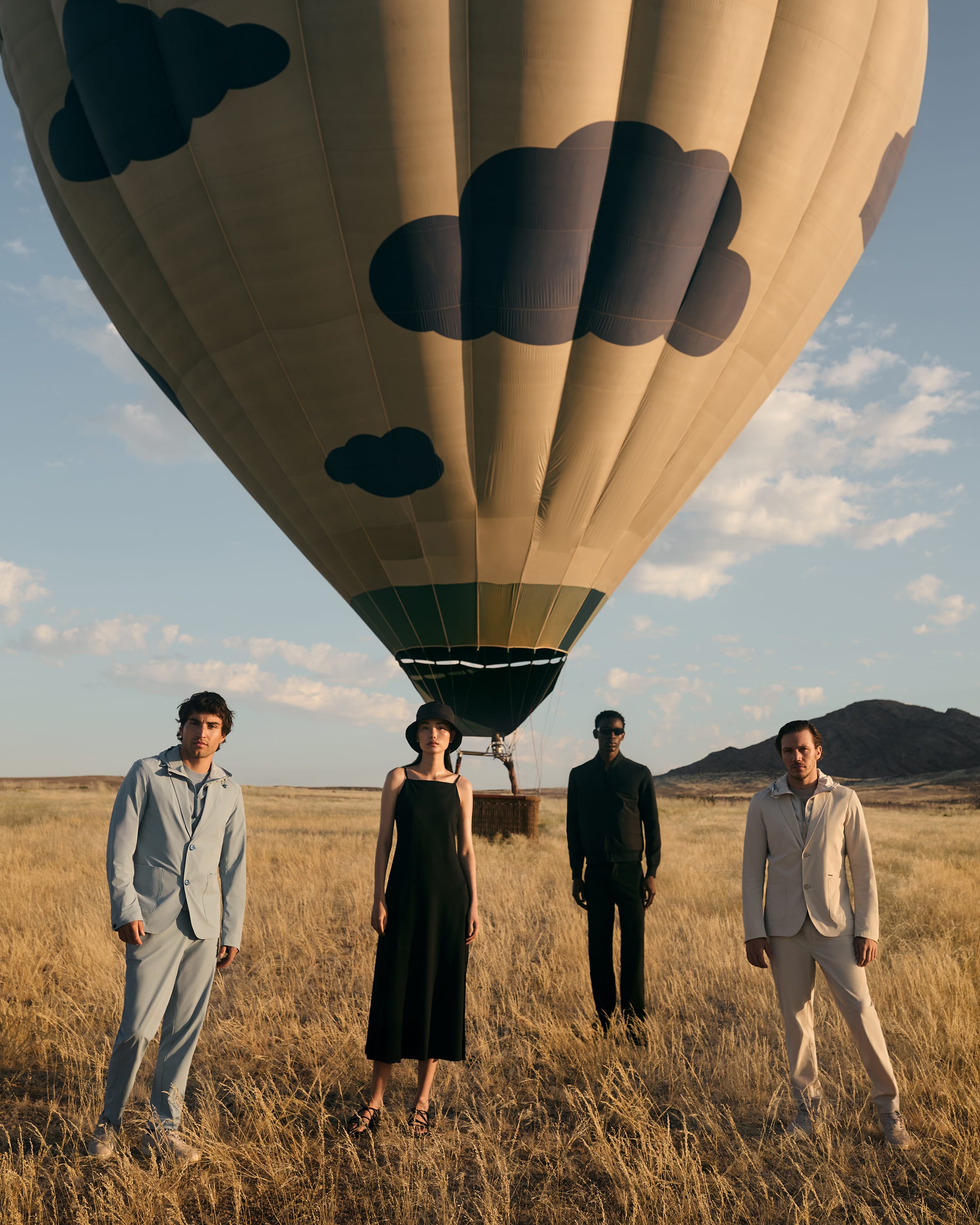 A woman and three men wear minimalist spring/summer outfits by AlphaTauri in a steppe.